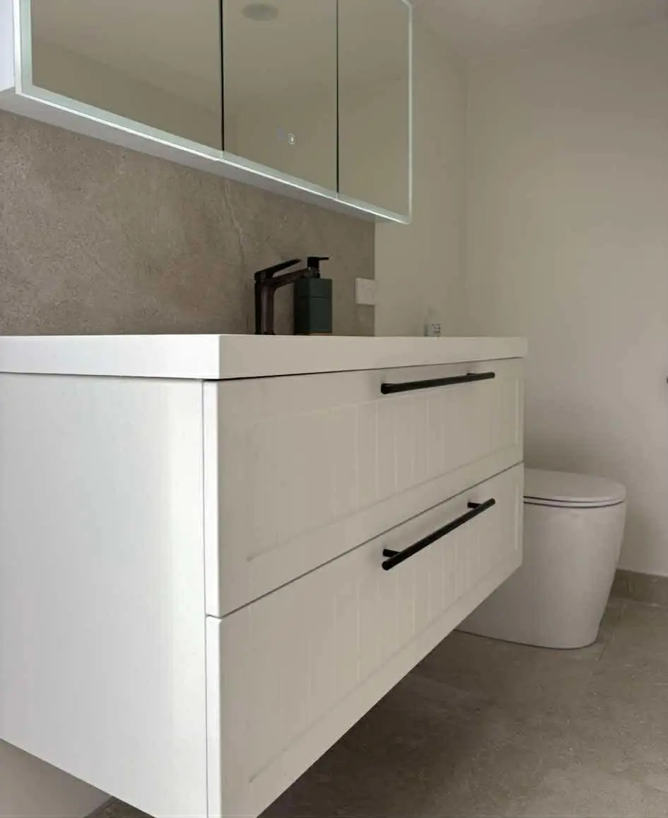 White floating vanity with black handles and a mirrored cabinet