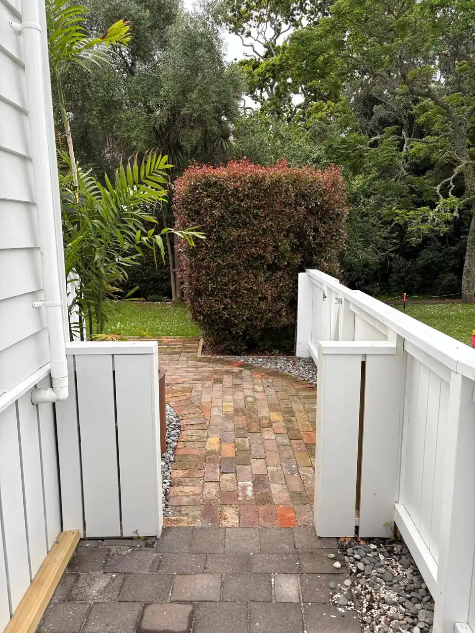 Brick path through white timber gates into a villa garden